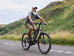 A senior citizen rides a mountain bike, e-bike, pedelec on a sloping road in a rural area, motion