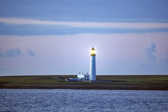 Lighthouse on the coast at dusk with blue sky in the background, crossing between Orkney and