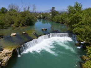 View of a waterfall and a river, surrounded by dense trees under a blue sky, aerial view, Manavgat