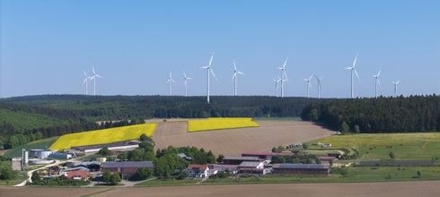 Landscape with wind turbines above agricultural fields and farms in front of a blue sky, near