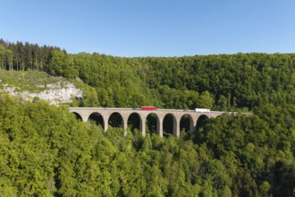 A viaduct stretches over a dense forest with vehicles on it, Drachenlochbrücke on the