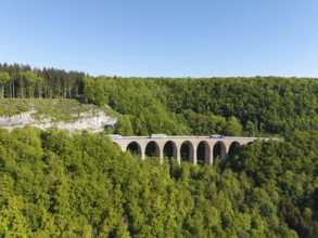 A viaduct spans a green forest while lorries pass the bridge, Drachenlochbrücke on the