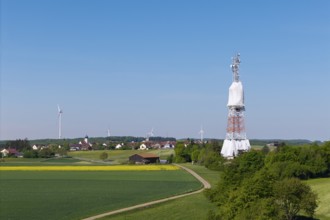 A transmission tower and wind turbines near a village under a blue sky, radio tower being
