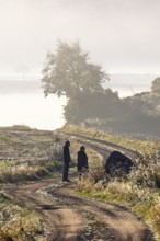 Two people walking on a winding gravel road in the countryside on a foggy autumn day