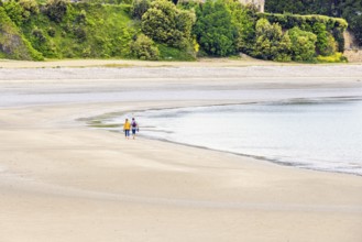 Two people walking at the waters edge on a sandy beach by the sea, Morgat, Crozon peninsula,