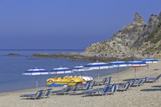 Beach with sunbeds and parasols in front of a rocky coast and blue sky, Ricadi, Capo Vaticano