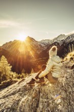 Woman sitting thoughtfully at a feslen at autumn atmosphere during sunset in the Swiss Alps in the