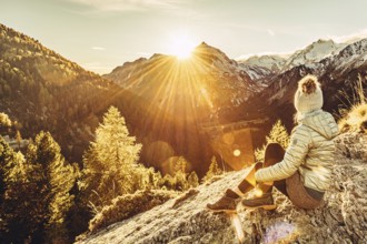 Woman sitting thoughtfully at a feslen at autumn atmosphere during sunset in the Swiss Alps in the