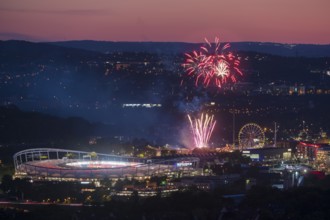 Fireworks at night illuminate the city above a stadium, next to an illuminated Ferris wheel in a