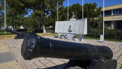 A monument with cannons and bust, surrounded by inscriptions and green vegetation in the open,