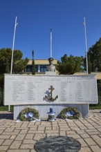 An open-air monument with bust and anchor, accompanied by plaques with inscriptions and wreaths,