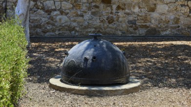 Bellini's Tower, Museum, An old black mine sits on a concrete foundation in front of a stone wall,