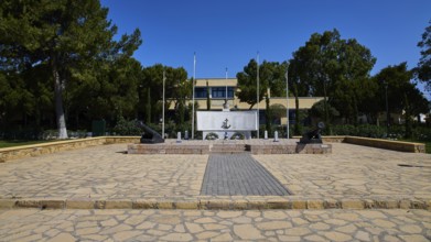 WW2, A memorial with cannons and flags stands on a paved square surrounded by trees, photos