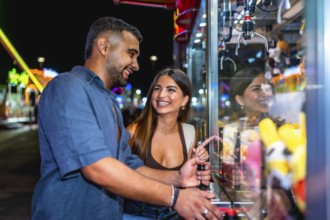 Young couple enjoying playful moments while trying to grab a prize from a brightly lit claw machine