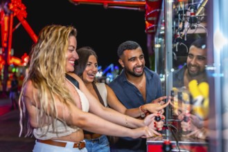 Happy friends enjoying a night out at amusement park, playing skill crane game and trying to win a