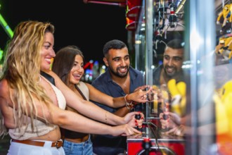 Group of friends having fun playing a crane game, trying to grab a prize, at an amusement park at