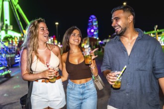 Three joyful friends walking and laughing together at an amusement park at night, enjoying colorful