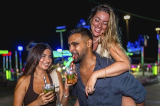 Group of cheerful friends enjoying cocktails and laughing together at an amusement park during a