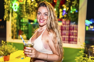 Young woman smiling and holding a refreshing cocktail at a vibrant night market, enjoying the