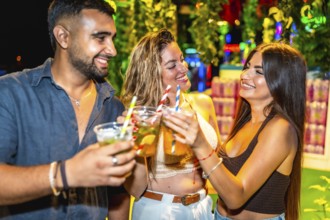 Happy friends enjoying drinks at open air bar, celebrating togetherness with cocktails under night