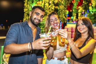 Three friends are raising their cocktail glasses for a celebratory toast, enjoying a vibrant