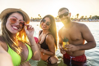 Young men and women having fun in the sea taking a selfie at sunset, enjoying refreshing cocktails
