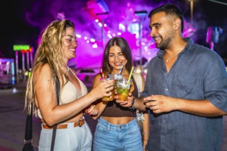 Three happy friends toasting non alcoholic drinks at night in amusement park, having fun together