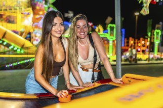 Two friends enjoying a game of air hockey at a brightly lit amusement park, adding excitement to