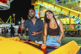 Young couple laughing and playing air hockey at an amusement park at night, enjoying their time