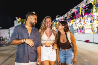Group of three young friends laughing and walking together in an amusement park, enjoying the