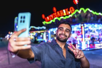 Happy young man smiling and taking a selfie while gesturing a peace sign, surrounded by vibrant