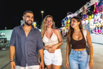 Three friends are enjoying their time together, strolling through a vibrant amusement park at night