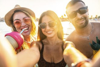 Group of cheerful multi ethnic friends taking selfie at beach party, enjoying refreshing drinks