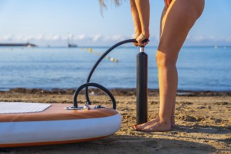 Woman inflating a paddleboard on a sandy beach, preparing for a summer paddle surfing session. Calm