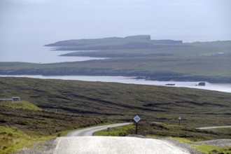 Coastal road winds through rolling countryside with views of the sea and distant islands, Eshaness,