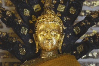 Buddha decorated with gold leaf, meditating under the protection of a seven-headed Naga snake, Phra