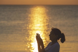 Woman, 40-50 years old, taking a photo with her smartphone at sunset, Koh Mook Island, Andaman Sea,
