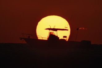 The sun rises behind a boat on the Costa Rei, a coastal stretch of the Italian Mediterranean island