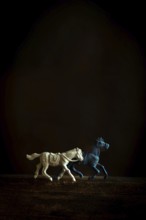 Two toy horses, one white and one blue, gallop side by side against a dark backdrop, capturing a