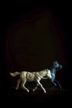 Two toy horses are captured in motion, one galloping energetically while the other walks gracefully