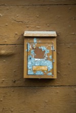 A weathered mailbox hangs on a rustic wooden wall, showcasing chipped paint in blue and brown tones