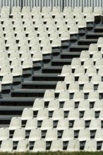 Empty white seats neatly arranged in rows await spectators at a stadium. The absence of an audience