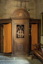 A beautifully crafted wooden confessional booth stands in a historic church, featuring ornate