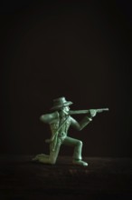 A detailed figurine of a gunslinger kneels and aims a rifle in a low light setting. Striking