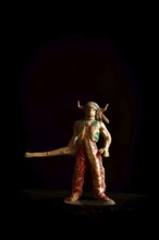 Vintage Native American Indian toy figure stands boldly in a dark setting, wielding a long weapon