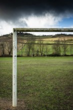 An old and weathered football goalpost stands empty on a green field, surrounded by a peaceful