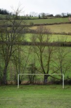 A serene countryside scene features two football goalposts set on a grassy field, bordered by