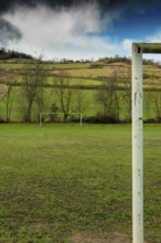 A football field is set against rolling hills and trees. The goalpost stands tall, framed by the