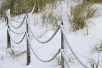 Winter day, onset of winter, demarcation poles with ropes in the snow-covered dune landscape of