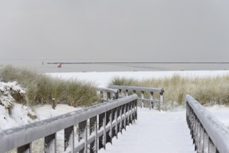 Winter day, onset of winter, wooden plank path leads through the snow-covered dune landscape to the